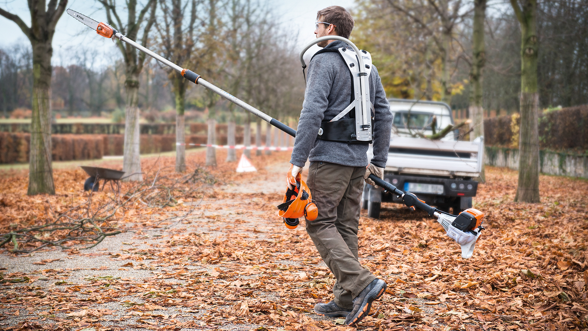 Homem com podadora em altura a gasolina STIHL HT 133 e veículo de trabalho no outono no parque