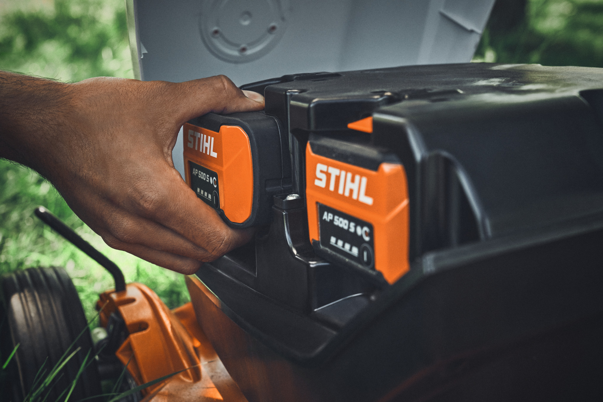 Una persona inserta una batería STIHL AP 500 S en un cortacésped de batería STIHL
