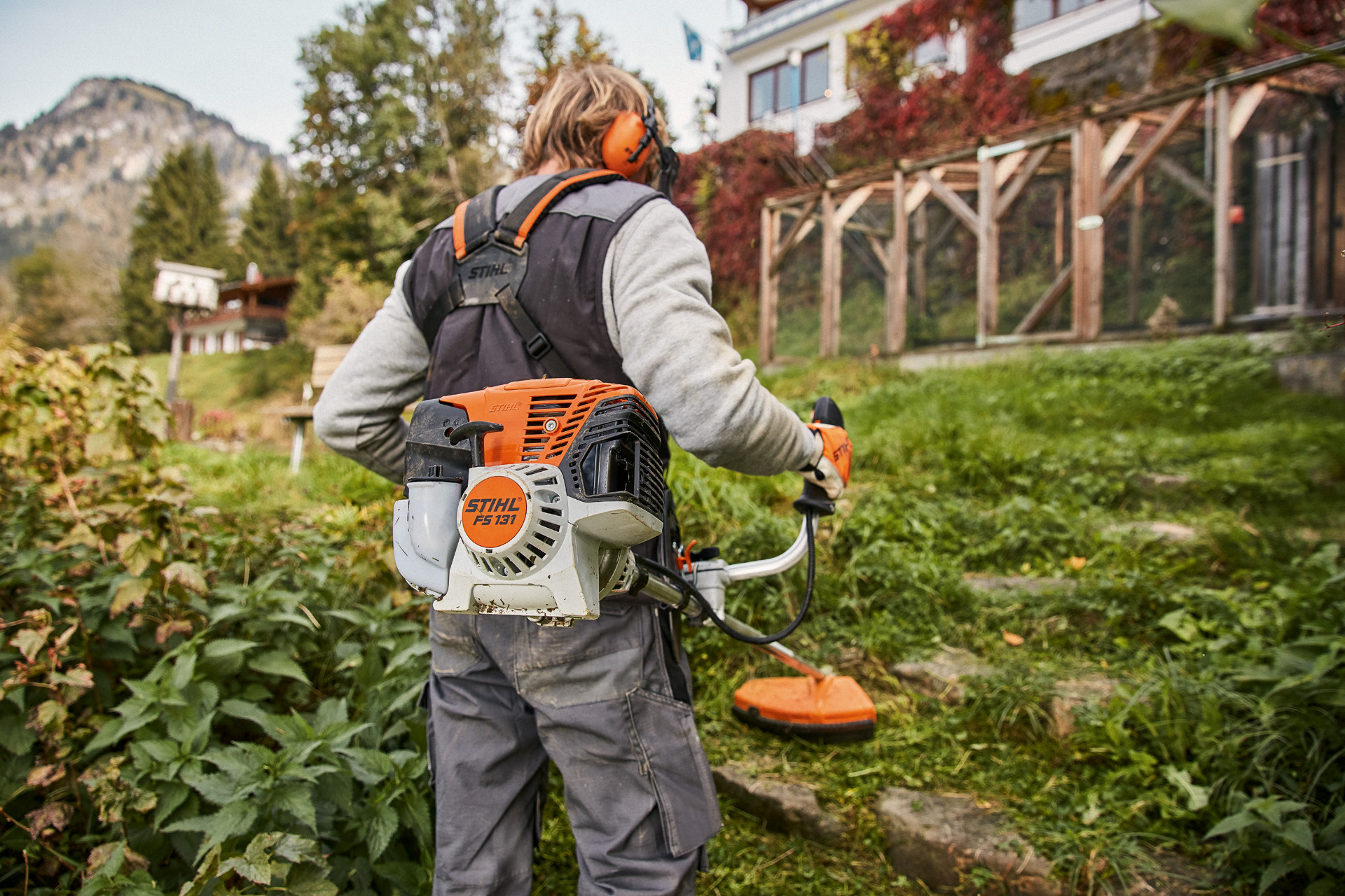 Un usuario con equipo de protección utiliza una desbrozadora de gasolina STIHL FS 131 en terrenos irregulares frente a una casa