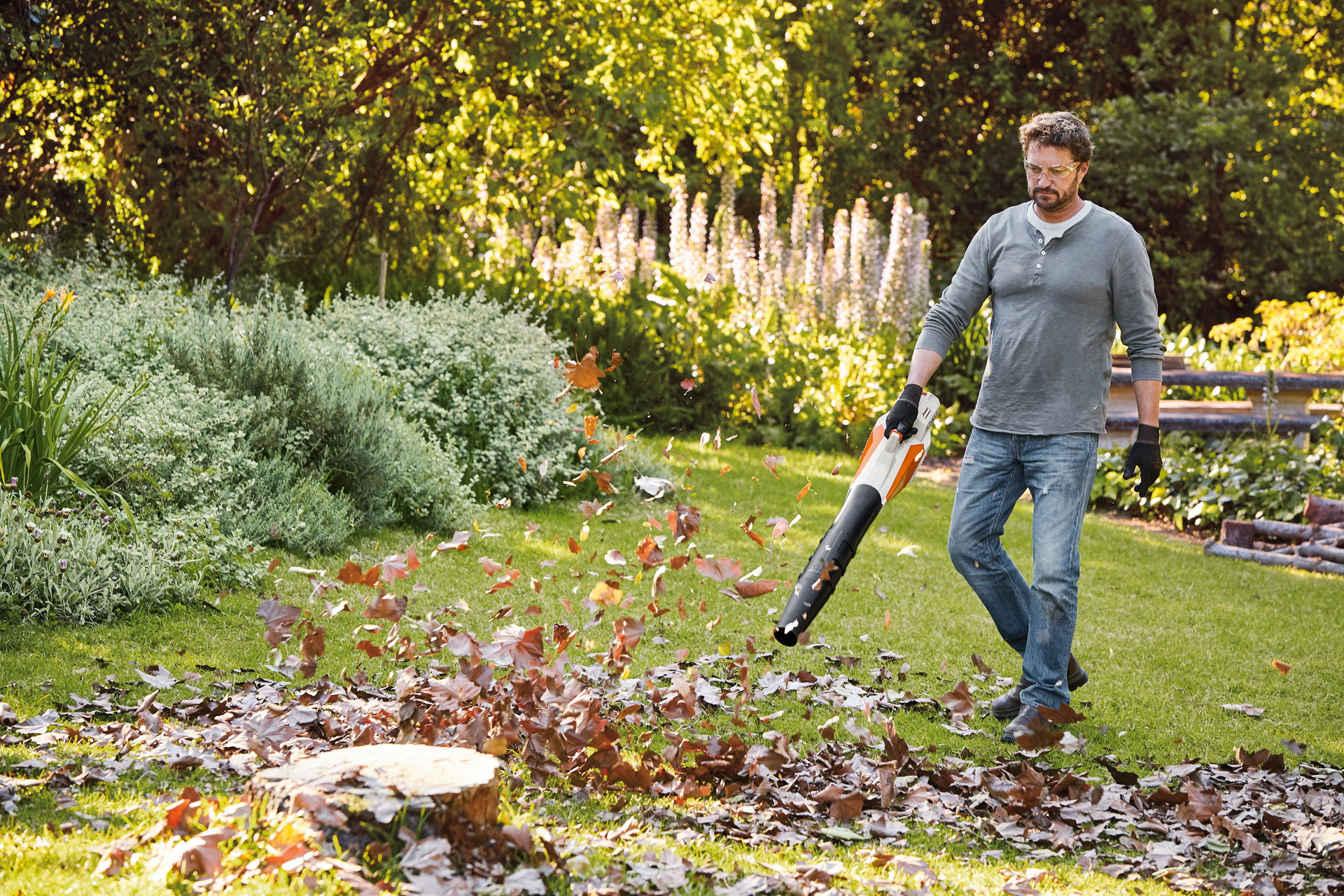 Un hombre sopla hojas en un jardín con un soplador a batería AK STIHL BGA 57